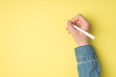 İzole edilmiş sarı zemin üzerinde beyaz kalem tutan bir kadının el fotoğrafı.