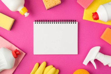 Açık ajanda temizleme pedlerinin, lastik eldivenlerin ve izole edilmiş pembe arka planda beyaz deterjan şişelerinin en üstteki fotoğrafı.