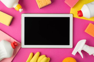 Süngerlerin ortasındaki tablet bilgisayarın en üst görüntüsü plastik eldivenler ve izole edilmiş pembe arka planda beyaz deterjan şişeleri