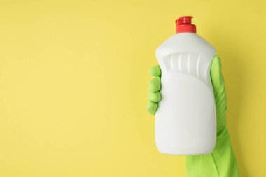 Sarı arka planda izole edilmiş ellerde deterjan resmi var.