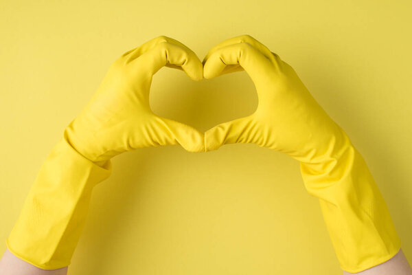 Top view photo of hands in yellow rubber gloves making heart with fingers on isolated yellow background with copyspace