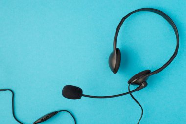 Üzerinde mikrofon bulunan siyah kablo kulaklığın üst görüntüsü izole edilmiş mavi arkaplan ve boş alan.