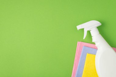 Beyaz sprey deterjan şişesinin üst görüntüsü etiketsiz, izole edilmiş yeşil arka planda, çok renkli yapışkan peçeteler ve boş alan