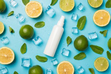 Ortadaki nane yapraklarında etiketsiz beyaz sprey şişesinin üst görüntüsü. Kesilmiş limon dilimleri, izole edilmiş açık mavi arka planda limon buzları ve su damlaları.