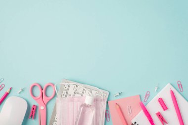Pembe kırtasiye kalemlerinin, kalemlerin, makasların, raptiyelerin, raptiyelerin, klavye fare dezenfektanlarının, izole edilmiş pastel mavi arka planda tıbbi yüz maskelerinin en üstteki resmi.