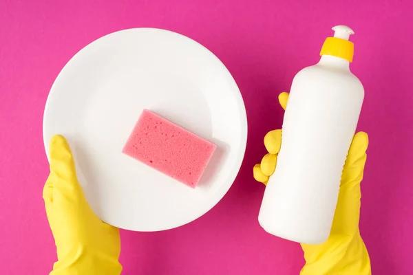 黄色橡胶手套手拿着白色洗涤剂瓶 没有标牌的白色干净盘子 粉红洗涤剂垫 带有彩色背景的顶部照片 — 图库照片