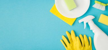 Plaka sünger sabun spreyi temizleme bezi ve mavi arka planda izole edilmiş sarı eldivenlerin üzerinde.