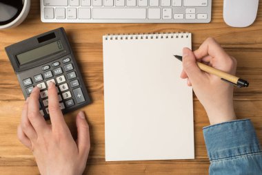 Kadın ellerinin hesap makinesine dokunduğu ve elinde kalemle izole edilmiş ahşap masa arka planında kahve fincanı tutan ilk kişi.