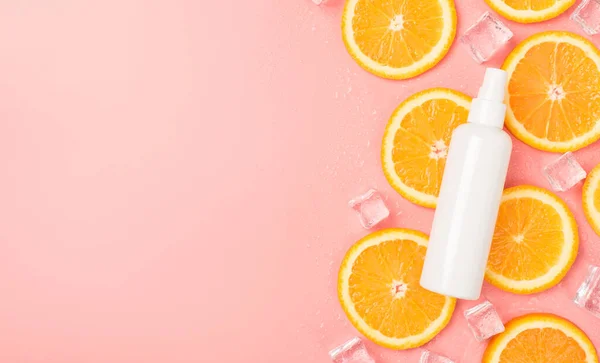 Top view photo of white spray bottle without label on orange slices ice cubes and water drops on isolated pastel pink background with blank space on the left