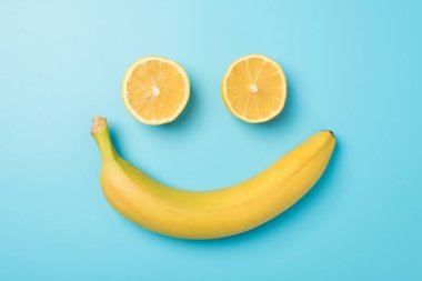 İki limon diliminden ve izole edilmiş açık mavi arka planda sarı muzdan yapılmış gülümseyen yüz fotoğrafı.