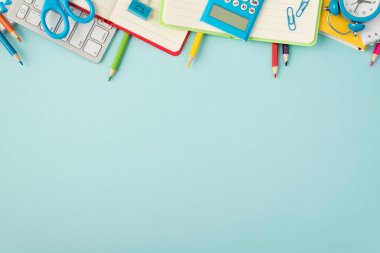 Klavye çok renkli kalemlerin üst görünümü kırmızı yeşil ve sarı günlükler raptiyeler makas bağlayıcı hesap makinesi ve izole edilmiş pastel mavi arkaplan üzerindeki alarm saati