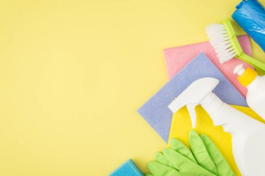 Çok renkli paçavraların en üstteki fotoğrafı lastik eldivenler mavi sünger çöp torbaları sprey ve izole edilmiş sarı arka planda izole edilmiş sarı renkli deterjan şişeleri.