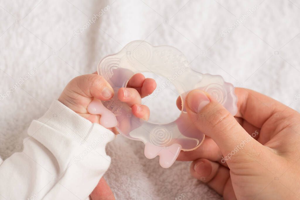 Closeup photo of baby's and mother's hands holding transparent teether toy lamb on isolated white textile background