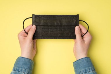 İzole edilmiş sarı arka planda, elinde siyah tıbbi maske olan bir kadının boş bir alanda çekilmiş ilk resmi.