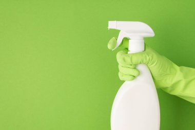 Elin yeşil lastik eldivenli profil fotoğrafı beyaz deterjan sprey şişesinde atomlaştırıcı kullanılarak izole edilmiş yeşil arka planda boş alan etiketi olmadan