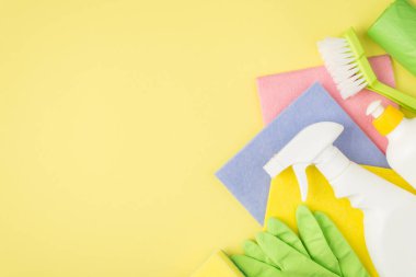 Çok renkli viskoz paçavralarının, lastik eldivenlerin, çöp poşetlerinin, izole edilmiş sarı arka planda jel deterjan şişelerinin üst görüntüsü.