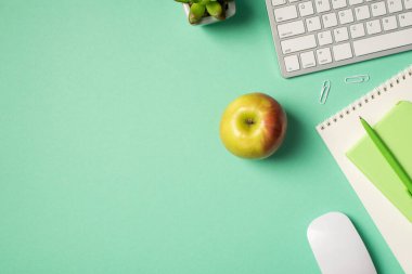 İki organizatörün üzerinde işyeri beyaz klavye fare kalemi, izole edilmiş turkuaz arka planda elma ve yerleştirme klipleri.