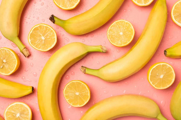 熟していないバナナのレモンの半分と水が孤立したパステルピンクの背景に落ちるのトップビュー写真 — ストック写真