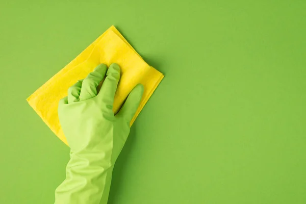 緑色のゴム手袋で手の写真右側のコピースペースと隔離された緑色の背景に黄色のラグで表面を拭く — ストック写真