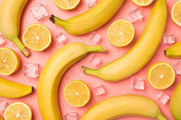 黄色の皮をむかないバナナの写真レモンの半分氷のキューブと水が孤立した光ピンクの背景に落ちる — ストック写真