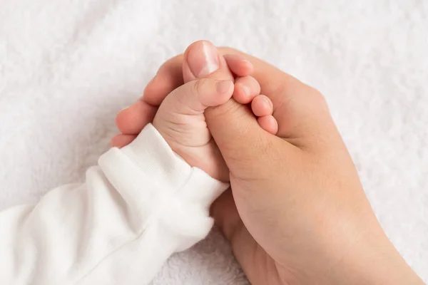 Closeup photo of newborn\'s tiny hand squeezing mother\'s thumb on isolated white textile background