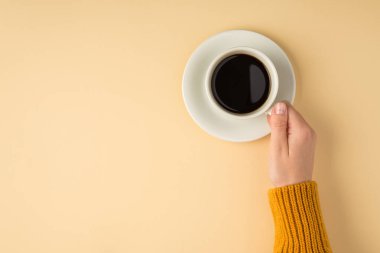 Sarı kazaklı bir kadının beyaz çay tabağının üzerinde beyaz bir fincan kahve tutarken çekilen ilk fotoğrafta izole edilmiş pastel turuncu arka plan ve fotokopi alanı