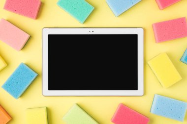 Ortadaki çok renkli tablet bilgisayarın üst görünüm fotoğrafı izole edilmiş sarı arkaplandaki süngerler ve telif boşluğu