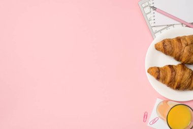 Tepede portakal suyu not defterinden yapılmış klavye fotoğrafı var. Kalem ataçları ve plaka ile birlikte iki kruvasan var.