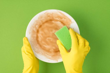 Sarı lastik eldivenli ellerin yeşil arka planda kirli tabak ve yeşil sünger tutarken en üstteki fotoğrafta.