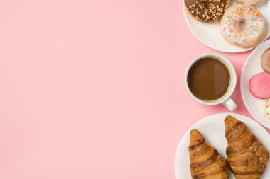 Üzerinde çeşitli hamur işi donut kruvasanları ve pembe arka planda izole edilmiş boş alan ile izole edilmiş bir fincan kahve resmi var.