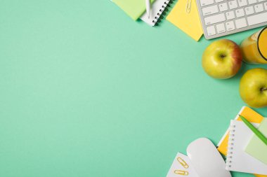 İşyeri klavye fare notları not defterlerinin üst görünümü. Kağıt kalemler, izole edilmiş turkuaz arka planda elma ve bardak meyve suyu tokuşturur.