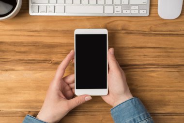 Akıllı telefon fincanı tutan ilk kişinin resmi... beyaz klavye ve fare... izole ahşap masa zemininde... kopyalanmış.