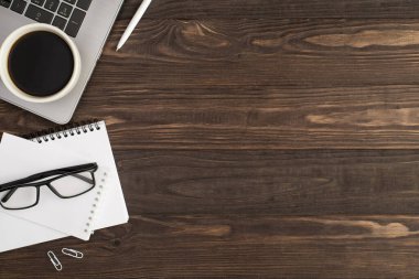 Dizüstü bilgisayardaki kahve fincanının üst görüntüsü beyaz ataçlar ve iki beyaz planlamacının gözlükleri izole edilmiş siyah tahta masa arka planında ve kopyalanmış alan