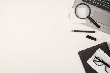 Dizüstü bilgisayardaki büyüteç yapıştırma etiketinin en üstteki fotoğrafı siyah kalem ve iki not defterindeki gözlük kopyalanmış beyaz tahta masa zemininde