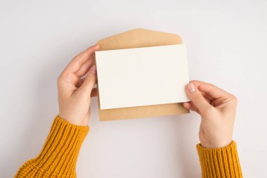 Sarı kazaklı bir kadının elinde açık el işi kağıt zarf ve beyaz bir kartın boş arkaplanda olduğu ilk kişi fotoğrafı.