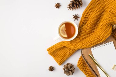 Portakal renkli kazaklı çay fincanının üst görüntüsü limon altın kalemli, deri çantalı ve kopyalanmış beyaz arka planda çam kozalaklı.