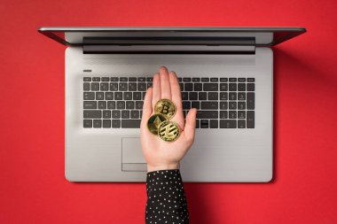 Üstten bakıldığında, uzanan el fotoğrafı bitcoin litekoin ve ruhani sembollerle izole edilmiş kırmızı arka planda gri dizüstü bilgisayarın üzerinde üç altın sikkeyi gösteriyor.