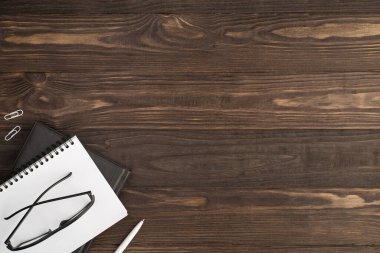 Beyaz raptiyelerin, kalemlerin ve gözlüklerin, izole edilmiş siyah tahta masa zemininde iki siyah ve beyaz defter üzerindeki en üstteki fotoğrafı.