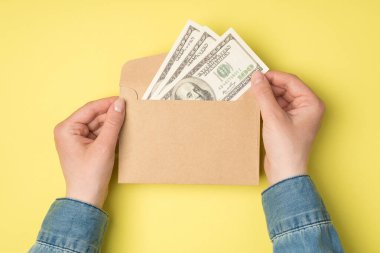 Kadın elinin açık el işi kağıt zarf tutarken çekilmiş ilk fotoğraf. Üzerinde 100 dolarlık banknotlar ve kopyalanmış sarı arka plan.
