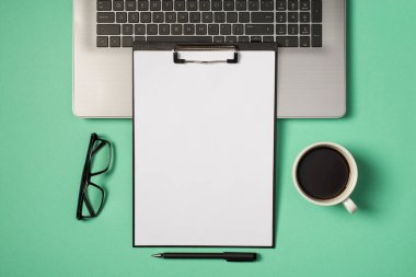 Laptop klavye bardaklarının üzerinde beyaz kağıt kağıtlar ve kopyalanmış turkuaz arka planda bir fincan kahvenin en üstteki görüntüsü.