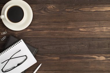 En üstteki fotoğrafta çay tabağı beyaz raptiyelerde içki fotografı. Kalem ve gözlük, izole edilmiş koyu renk tahta masa arka planında iki kopya kitabı. Boş alan.