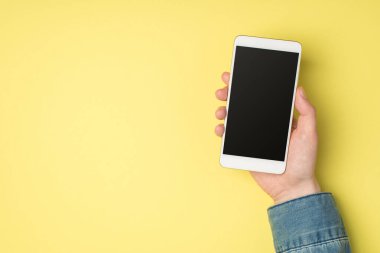 Tepedeki fotoğrafta kadının elinde akıllı telefon görüntüsü var. Kopyalama alanı olan izole edilmiş sarı arkaplan üzerinde.