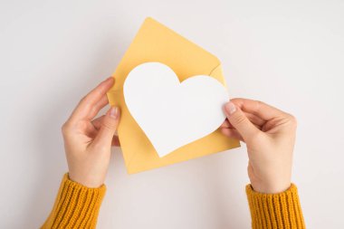 Sarı kazaklı, açık bir zarf tutan kadın elleri ve boş bir arkaplan ile izole edilmiş beyaz arkaplan üzerine beyaz kağıt kalp.