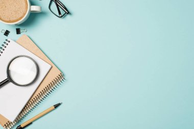 İş yeri planlayıcılarının en iyi görüntüsü kalem klasörleri büyüteç bardakları ve izole açık mavi arka planda bir fincan köpüklü kahve.