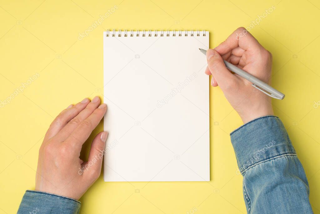 First person top view photo of female hands holding pen over open planner on isolated yellow background with blank space