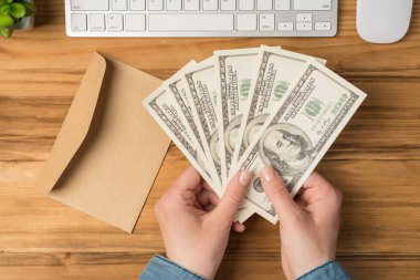 Kadın ellerinin para yelpazesini tutarken çekilmiş ilk fotoğrafı 100 dolarlık banknotlar açık el işi kağıt zarf izole edilmiş tahta masa arka planına beyaz klavye ve fare yerleştirin