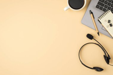 Gri dizüstü bilgisayarlı not defterinin üstünde ataç kulaklıklar ve bej arka planda izole edilmiş boş alan ile izole edilmiş bir fincan kahve.