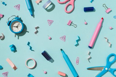 Çift renkli mavi ve pembe okul aksesuarlarının üst görüntüsü kağıt kalem bağlayıcı raptiye silgi yapışkan bant makası ve izole pastel mavi arka planda alarm saati.