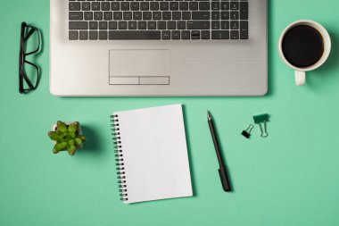 Dizüstü bilgisayarın klavye gözlüklerinin en üst görüntüsü yeşil ve siyah klasör klipleri boş arkaplan ile izole edilmiş turkuaz arka planda bitki kalem ve spiral hatırlatıcı