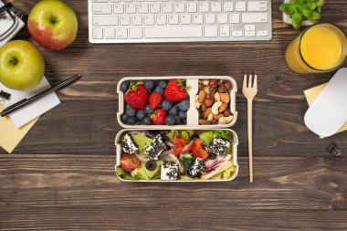 Çalışma alanının en iyi fotoğrafı sağlıklı yiyecek çatalı iki tane salata böğürtlenli beslenme çantası fındık kırtasiyesi fare elması meyve suyu bardağı ve izole edilmiş siyah ahşap masa arkasında saksı.